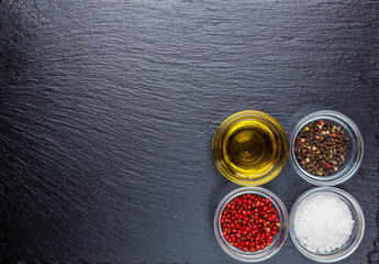 Olive oil, salt, pepper, on a black slate stone board. Food background