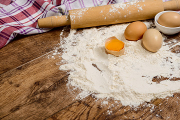 Flour, eggs, salt, towel, rolling pin on wooden table ready for cooking
