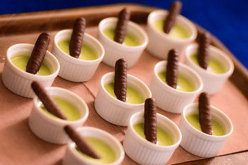 Small bowls of mint ice cream with long chocolate biscuit on a brown tray