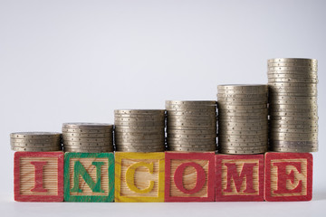 INCOME text written on wooden blocks with stacked silver coins isolated on white background.Income increase concept with upward pile of coins.