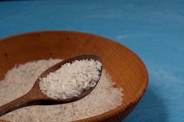 Raw rice in wooden bowl with wooden spoon on blue background