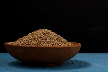 Wooden bowl with pearl barley on blue and black background. Close-up.