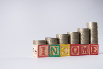 INCOME text written on wooden blocks with stacked silver coins isolated on white background.Income increase concept with upward pile of coins.
