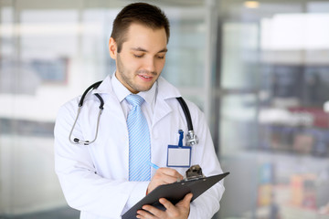 Male doctor filling up medical form while standing upright in hospital. © volha_r