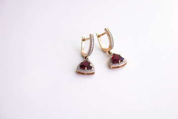 Gold earrings with red precious stone and small diamonds on a white background