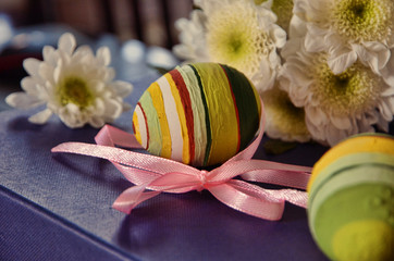 Easter holiday. A branch of white chrysanthemum and a ceramic cup with dyed eggs on a blue background. Bright colors of Easter. Bizarre egg staining on Easter
