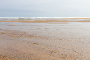 Detalle de ancha llanura de playa vacía con arena clara mojada y las olas del mar llegando suavemente
