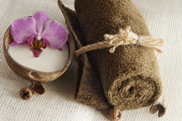 A folded towel and an orchid flower in milk in a coconut on a light woven napkin, preparation for...