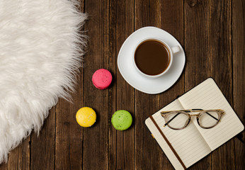 Coffee mug, macarons, notebook and glasses on a wooden table. Top view