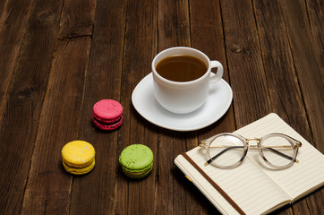 Coffee mug, macarons, notebook and glasses on a wooden table. Side view