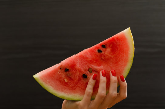 Semicircle of ripe watermelon in female hand on a black background,  space for text