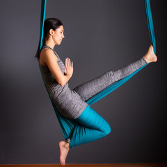 young beautiful brunette woman doing fly yoga. Sitting in hammock with namaste gesture. Wellness...