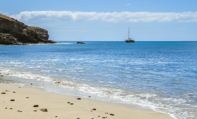 Beach, volcanic dark stones, a boat and blue sky