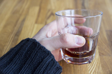 At wooden table male hand hold glass with alcohol