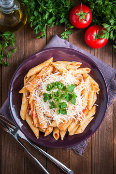 Penne pasta with chicken, tomato sauce, parmesan cheese and parsley on dark wooden background top view. Italian cuisine.