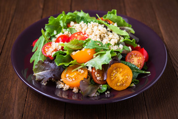 Fresh healthy salad with quinoa, cherry tomatoes and mixed greens (arugula, mesclun, mache) on wood background close up. Food and health. Superfood meal.