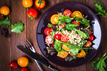 Fresh healthy salad with quinoa, cherry tomatoes and mixed greens (arugula, mesclun, mache) on wood background top view. Food and health. Superfood meal.