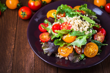 Fresh healthy salad with quinoa, cherry tomatoes and mixed greens (arugula, mesclun, mache) on wood background close up. Food and health. Superfood meal.