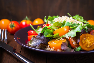 Fresh healthy salad with quinoa, cherry tomatoes and mixed greens (arugula, mesclun, mache) on wood background close up. Food and health. Superfood meal.