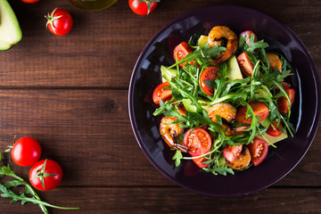 Fresh salad plate with shrimp, tomato, avocado and arugula (salad rocket) on wooden background top view. Healthy food. Clean eating.