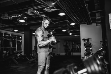 Handsome muscular man is working out and posing with dumbbells at a gym