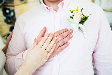 Wedding boutonniere on suit of groom and bride’s hand
