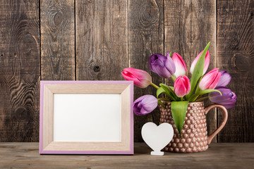 Fresh colorful tulips, white heart and blank wooden frame