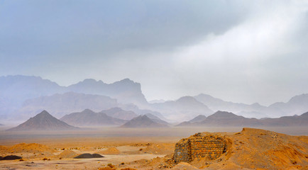 desert area in the central part of Iran, on a background towers a mountain chain, in the sky rain clouds