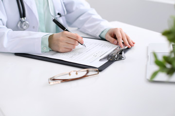 Close-up of a female doctor filling  out application form , sitting at the table in the hospital