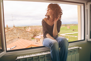 Mujer joven sentada en una ventana con unas vistas a un pueblo de fondo 