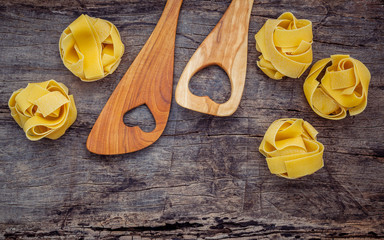 Italian foods concept and menu design. Dried homemade Fettuccine with heart shaped wooden spatula set up on shabby wooden background with flat lay and copy space.