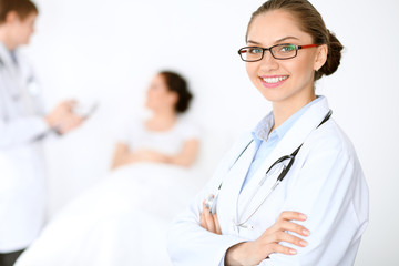 Cheerful smiling female doctor on the background with physician and his patient in the bed. High level and quality of medical service concept.