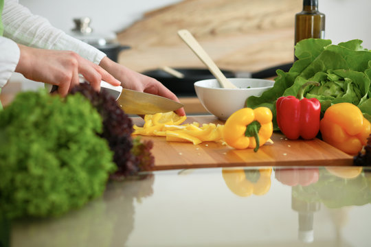 Closeup of human hands cooking vegetables salad in kitchen on the glassr table with reflection. Healthy meal and vegetarian concept