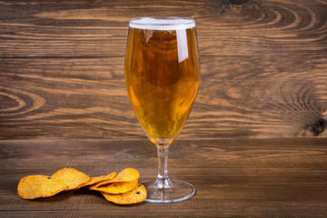 Lager beer in glass and potato chips on wooden background