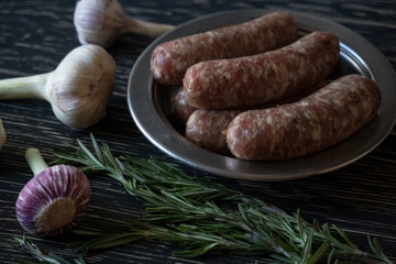 Raw sausages with garlic, rosemary on wooden surface