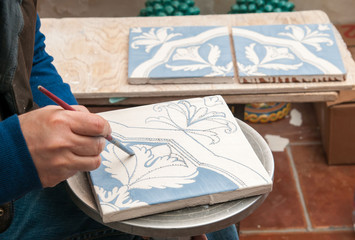 Pottery artisan in Caltagirone, Sicily, decorating just enamelled square tiles in his work table - 142744221