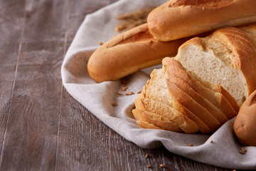 Slices of white bread and baguette laying on white cloth with gradient dark-brown background