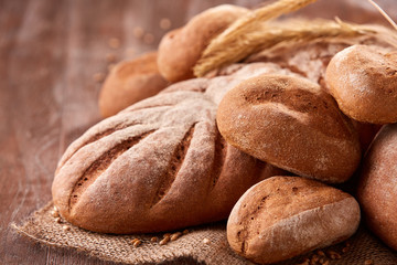 handmade tasty bread lying on burlap on the wooden table with flour, wheat and ears of wheat