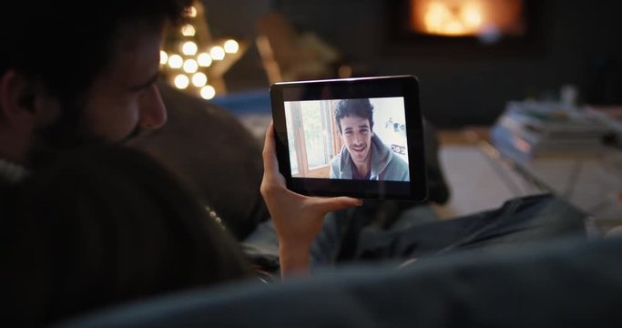 Young couple having video chat at home in front of fireplace holding smartphone webcam chatting to friend