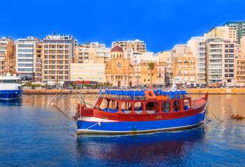 Beautiful traditional architecture and a classical boat on the famous harbor of Malta, at sunset