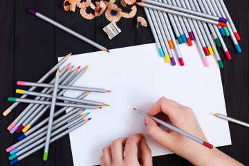 Artist hands holding color pencil and blank sheet of paper