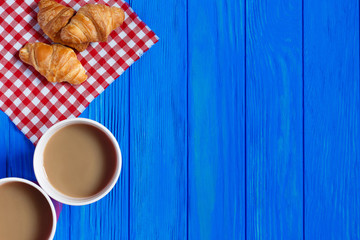 Two cups of coffee and croissants on blue wooden table