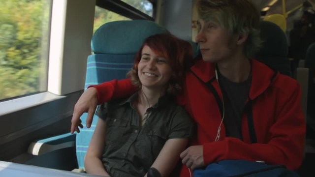 Young beautiful happy hipster couple riding by the train, talking about their life, laughing and joking. Summer vacation.
