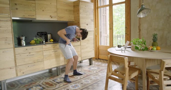 Creative Young Man Dancing In Kitchen Making Homemade Food In The Morning Listening To Music On Smartphone And Coffee At Home