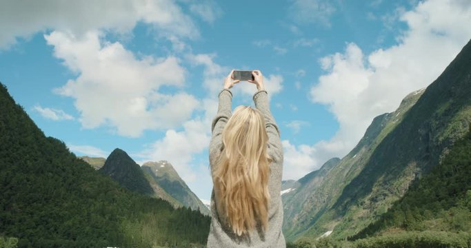 Woman wearing grey sweater taking photograph beautiful mountain with smartphone photographing scenic landscape nature background view enjoying vacation travel adventure