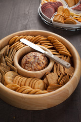Cheese ball with various crackers and sliced meat and cheese on dark wooden background slightly angled shot