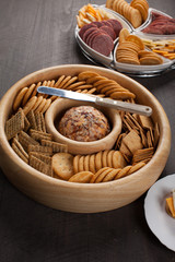 Cheese ball with various crackers and sliced meat and cheese on dark wooden background vertical shot