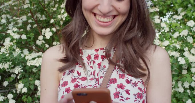 Social media woman holding smartphone sending text message snapchat in front of flowers wearing cute summer dress in spring
