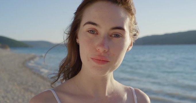 Close up portrait of beautiful young woman running hand through hair blowing in wind on tropical beach slow motion