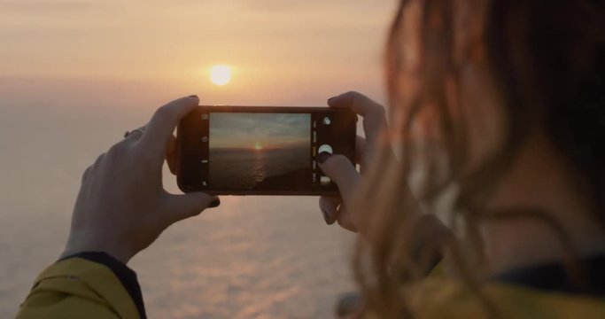 Close up Woman photographing sunset with smartphone Girl taking photo hair blowing over ocean view with soft light lens flare landscape nature background enjoying vacation travel adventure 